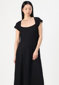 Zwarte linnen jurk met een vierkante halslijn, korte kapmouwen en een vloeiende A-lijn silhouette. Bevat subtiele naaddetails en een soepele textuur.