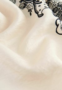 Țesătură ușoară de culoare crem, cu modele florale negre complicate și textură netedă, evidențiază drapajul elegant.