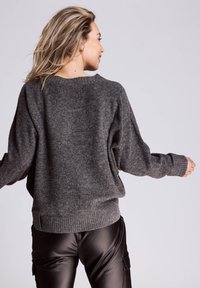 Grauer Strickpullover mit weiter Passform, weiten Ärmeln, geripptem Saum und Bündchen, kombiniert mit schwarzen Lederhosen. Strukturierte Stoffoberfläche sichtbar.