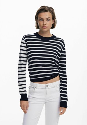 Navy and white striped knit sweater with a crew neck and long sleeves; cropped design with ribbed cuffs and hem. Paired with white jeans.