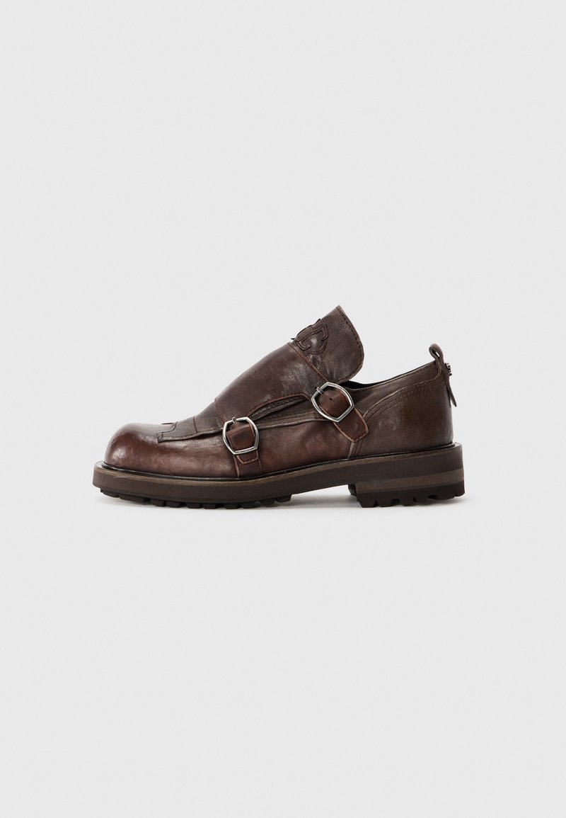 Brun läder slip-on sko med två metallspännen, rund tå och strukturerad yta på en stabil gummisula.