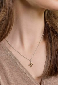 Collana in argento con un pendente floreale decorato con quattro pietre color ambra e dettagli metallici intricati, poggiata su un maglione beige.