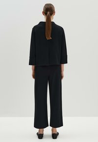 Haut noir à manches longues avec col et dos fendu, associé à un pantalon à jambes larges. Texture lisse, design minimal, porté avec des chaussures à talons.