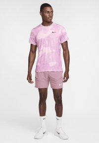 Camiseta deportiva de Nike en color rosa, con un patrón abstracto, mangas cortas y un diseño ajustado, combinada con pantalones cortos rosa claro y zapatillas blancas.