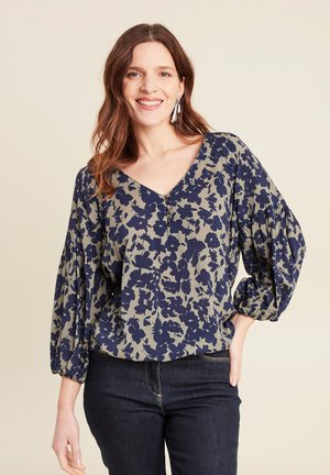 Blumenbluse mit V-Ausschnitt, olivgrünem Grundton und marineblauem Blumenmuster sowie Puffärmeln. Strukturierter Stoff mit Knopfdetails.