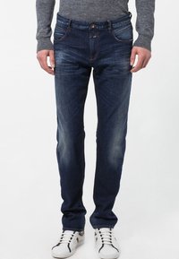 Mörkblå denimjeans med slim fit, fem fickor och subtila blekningar vid låren, tillsammans med vita sneakers.