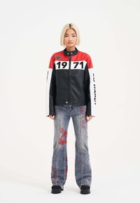 Chaqueta de cuero negra y roja con mangas blancas, que presenta el número "1971". Combinada con unos jeans acampanados azules con detalles bordados en rojo.