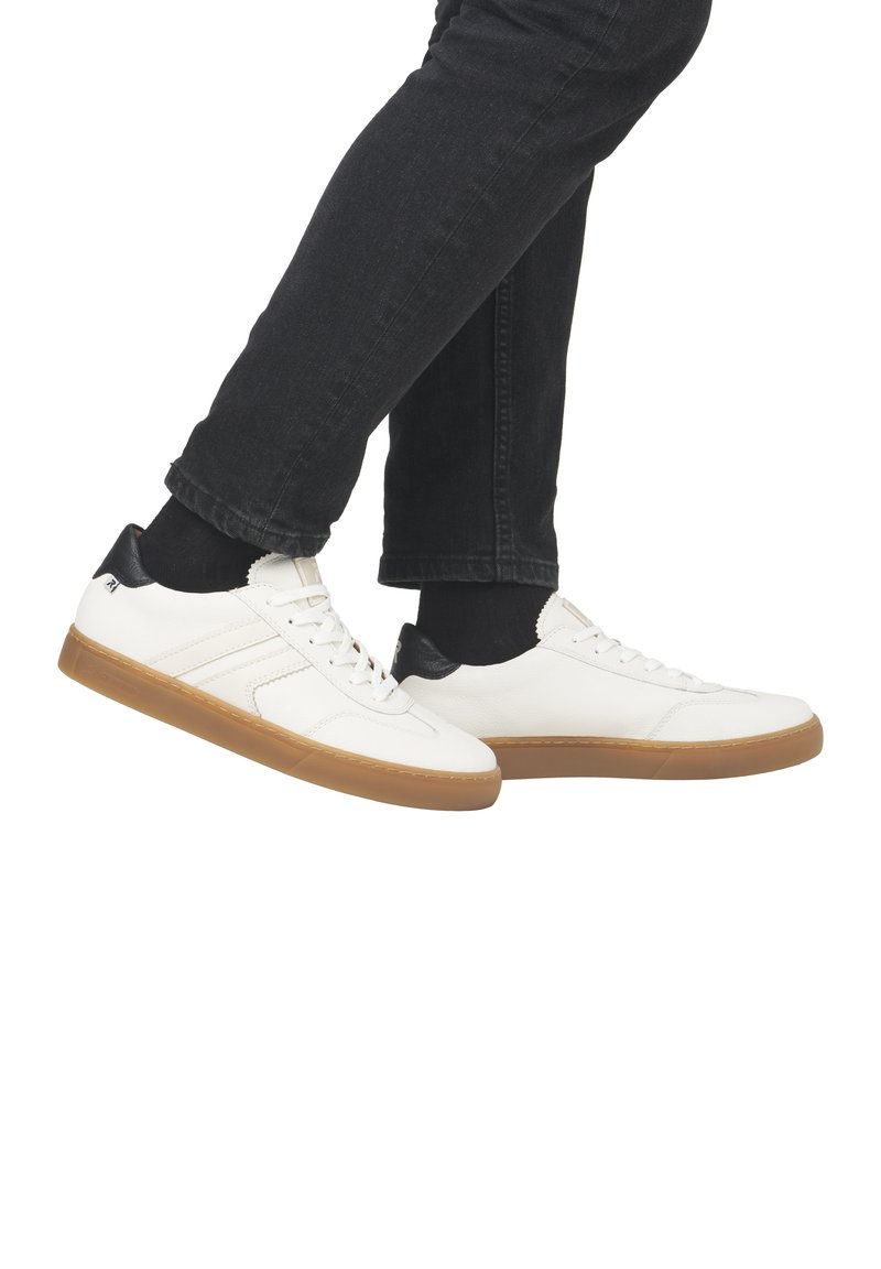 Sneaker in pelle bianca con accenti neri sul tallone, caratterizzate da una superficie liscia e una suola in gomma, presentate con pantaloni in denim scuro.