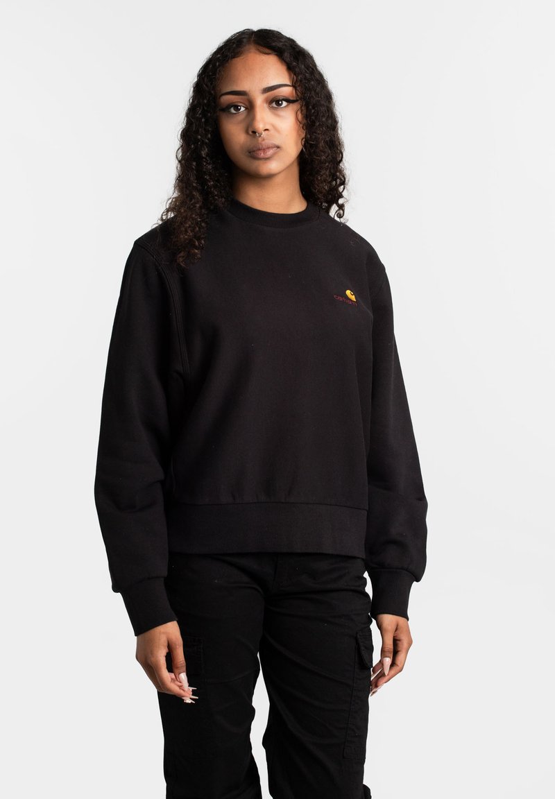 Zwarte sweatshirt met een geribbelde ronde hals, lange mouwen en een relaxte pasvorm. Heeft een klein logo in geel en rood op de borst.