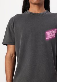 Grå bomulds t-shirt med rund hals og korte ærmer. Har et neongult logo med teksten "TOMMY JEANS" på venstre brystområde.