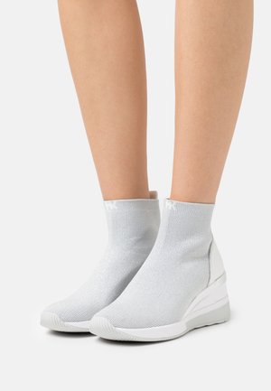Chaussures argentées à hauteur de cheville avec une tige tricotée et une semelle compensée. Elles présentent une texture lisse et un ajustement élastique autour de la cheville.