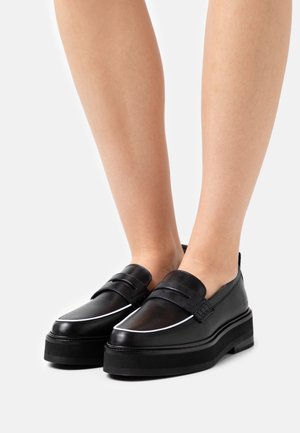 Mocassins en cuir noir avec deux bandes décoratives, semelle plateforme surélevée et passepoil blanc le long du bord supérieur. Texture lisse.