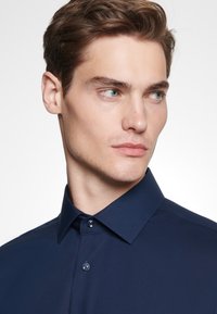 Navyblauw overhemd met knopen, voorzien van een frisse kraag, een gladde textuur en een subtiele glans. Heeft bijpassende knopen en een getailleerde pasvorm.