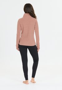 Langärmeliges, hellrosa Oberteil mit hohem Kragen und Daumenlöchern, kombiniert mit enganliegenden schwarzen Leggings. Glatte Texturen, minimalistisches Design.