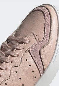 Las zapatillas de cuero rosa presentan una parte superior texturizada, un diseño perforado y cordones planos. Los acentos incluyen un panel de ante y costuras en contraste.