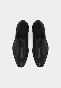 Ζευγάρι μαύρα δερμάτινα παπούτσια με κορδόνια, φωτογραφημένα από πάνω σε απλό λευκό φόντο.