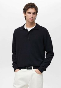 Black knit pullover with a collar, three-button placket, and ribbed cuffs. Worn with white pants. Smooth texture, casual design.