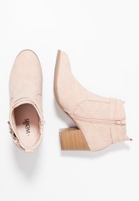 Bottines rose blush avec un design perforé, fermeture éclair sur le côté et un talon bloc empilé. Fabriquées en matériau doux semblable au daim.
