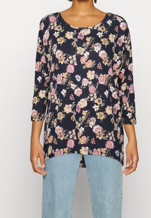Navy blue floral long-sleeve top with pink, yellow, and white flowers worn with light blue jeans.