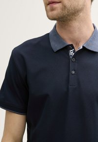 Námornícky polo tričko s textúrovaným kontrastným golierom. Obsahuje tri gombíky, krátke rukávy a hladké tkaninové spracovanie.