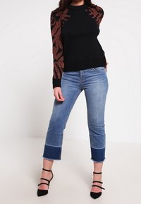 Svart stickad tröja med rödbruna mönstrade ärmar, tillsammans med ljusblå cropped jeans med fransad nederkant och tvåfärgad design.