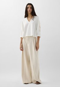 Top blanc court à col en V avec des détails floraux sur les manches, assorti à un pantalon large taille haute beige en tissu texturé.