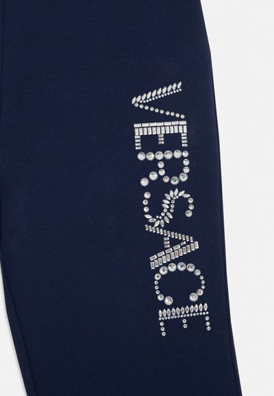 Tela azul marino con finos cristales plateados decorativos dispuestos para deletrear "VERSACE" en un diseño vertical en la ropa.