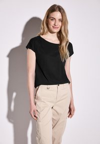 Top nero a maniche corte con scollatura tonda e pieghe sottili. Abbinato a pantaloni beige chiaro con vita sicura e dettagli con tasche.
