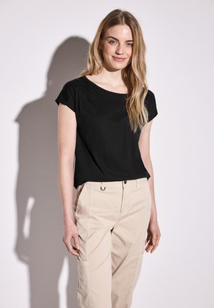 Zwarte korte mouw top met een ronde halslijn en subtiele plooien. Gecombineerd met lichtbeige broek met een veilige tailleband en pocketdetails.
