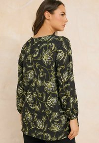 Maglietta a maniche lunghe in tessuto nero con motivo floreale verde. Collo rotondo, vestibilità morbida e polsini arricciati per un tocco di dettaglio.