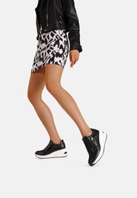 Sneakers in pelle nera con suola a zeppa bianca, caratterizzati da dettagli con cerniera e un design elegante, abbinati a una gonna a fantasia.