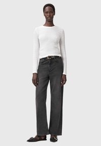 Witte lange mouwen top van textuurstof, gecombineerd met hoge, wijde zwarte jeans en zwarte flats met een gouden gesp detail.