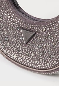 Paarse stoffen tas versierd met rhinestones in verschillende maten, met een driehoekig Guess-logo in het zwart. Ritssluiting aan de bovenkant.