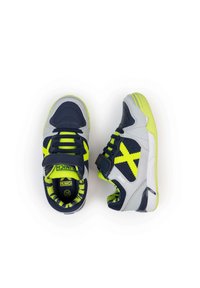 Zapatos deportivos en gris, azul marino y verde brillante. Presentan una parte superior de malla con un patrón en X, cuello acolchado y correa de gancho y bucle.