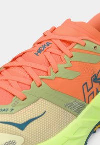 Bright coral and green Hoka running shoe with detailed mesh upper, neon yellow sole, and laces tied across the top.
