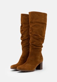 Brązowe zamszowe kozaki do kolan o luźnym fasonie, z okrągłym noskiem i słupkowym obcasem, z teksturowanym wzorem na obcasie.