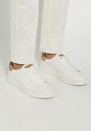 White leather sneakers with a smooth texture and light brown suede accents at the heel. Features a rounded toe and flat rubber sole.
