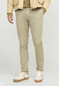 Beżowe spodnie slim-fit wykonane z gładkiej bawełny, w połączeniu z białymi trampkami z brązową podeszwą i subtelnymi akcentami.