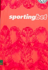 Camiseta atlética roja con un patrón floral texturizado, logo de "sportingbet" en blanco y una etiqueta verde de Puma en la parte inferior izquierda.