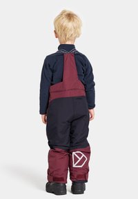 Röd och marinblå vattentät snowsuit med justerbara axelremmar, med en präglad logotyp på sidan och elastiska manschetter vid anklarna.