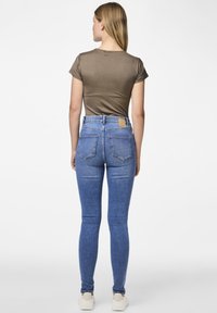 Jean skinny en denim bleu clair avec une taille haute, cinq poches et une étiquette en cuir marron à l'arrière. Top court à manches courtes en olive.