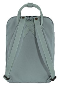 Un sac à dos gris clair avec une texture lisse et mate, doté de sangles tissées réglables et d'une poignée sur le dessus pour le transport. Fermeture à glissière en haut.