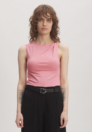 Rosa mouwloos topje met een ronde halslijn en een draai-detail op de schouder, gecombineerd met hoge zwarte broeken en een zwarte riem.