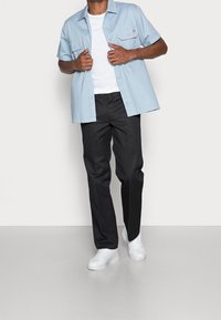 Jasnoniebieska koszula z krótkim rękawem z bawełny z dwoma kieszeniami na piersi, zestawiona z czarnymi spodniami i białymi trampkami. Prosty, czysty design.