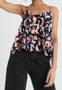 Haut sans manches à motif floral en rose, noir et bleu. Présente un design à plusieurs niveaux et des bretelles spaghetti ajustables. Associe avec un pantalon noir.