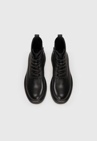 Botas de tobillo de piel negra con superficie texturizada, parte delantera con cordones y cremallera lateral. Punta redonda y suelas gruesas. Diseñadas para la durabilidad.