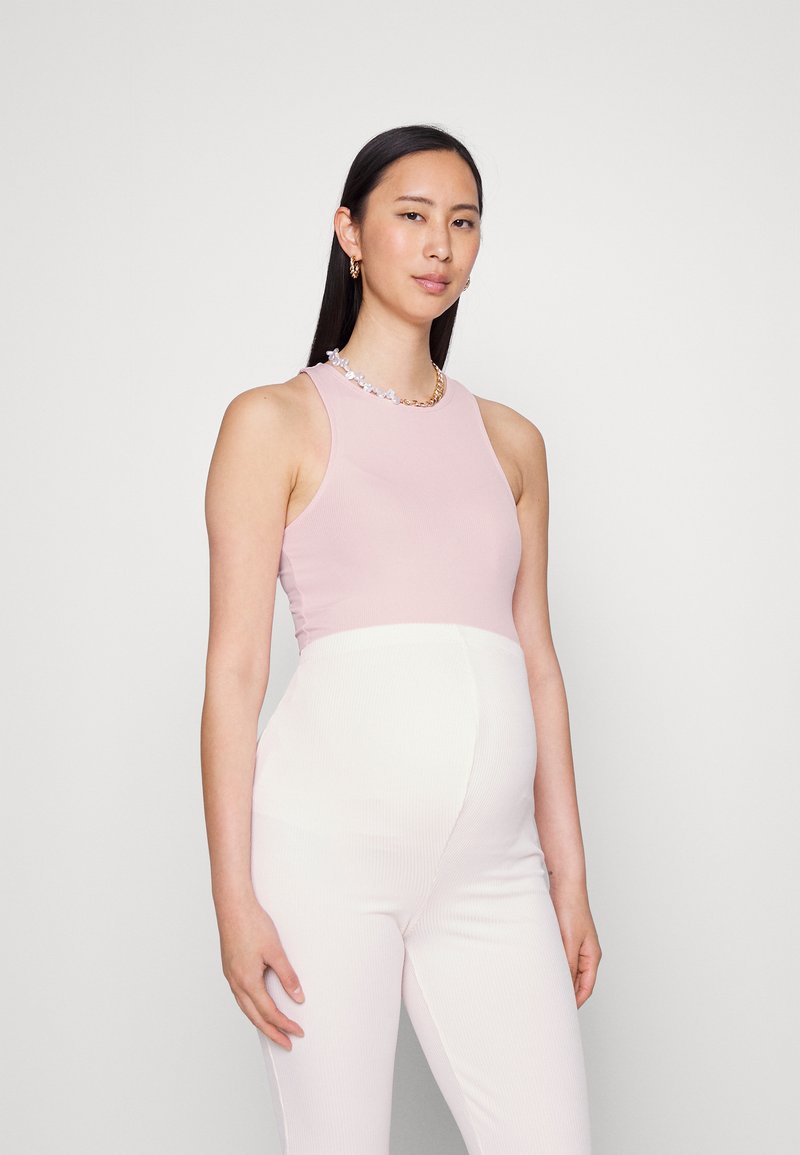 Top de alças ribbed rosa com decote redondo, combinado com calças de maternidade brancas ribbed. Detalhe notável em corrente e flores no decote.