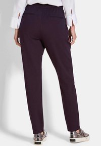 Paarse broek met een gladde textuur, elastische taille, en twee achterzakken, gecombineerd met metallic sneakers.