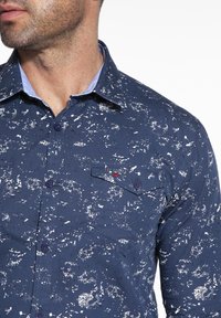 Námořnická modrá košile na knoflíky s rozstříknutým vzorem, se světle modrým límečkem, kapsou na prsou a značkovou visačkou. Vyrobena z hladkého materiálu.