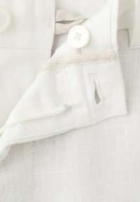 Witte linnen kledingstuk tailleband met genaaide knoop en knoopsgat detail op een gestructureerde stoffen achtergrond.